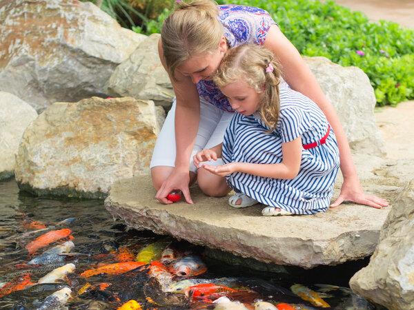 Woman,And,Daughter,Feeding,Fishes,In,Pond.